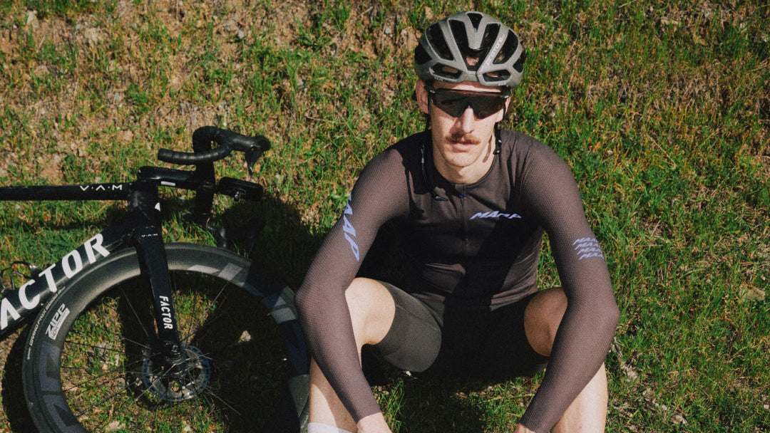 Cyclist in black outfit sitting on grass next to a bicycle