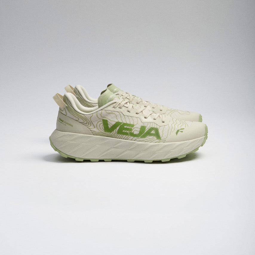 A pair of Hoka Veja running shoes in a light cream and sage green colorway, shown from a side profile against a neutral gray studio background.