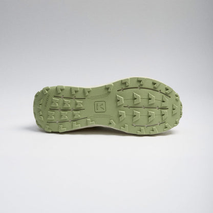 The outsole of a green shoe, showing a textured tread pattern and a small embossed logo, photographed against a neutral gray studio background.