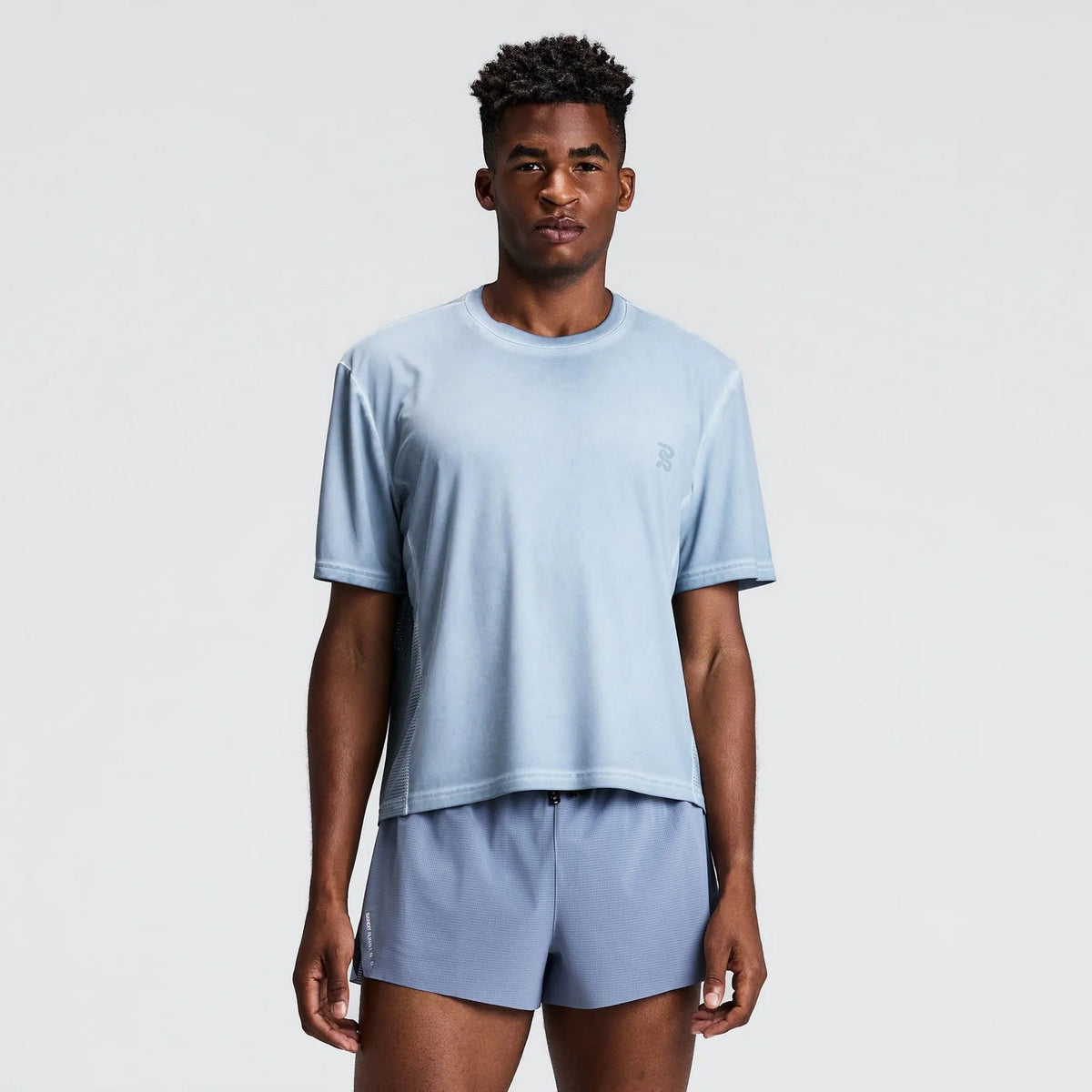 A man modeling a light blue short-sleeve crewneck t-shirt and matching light blue shorts against a plain light gray studio background.