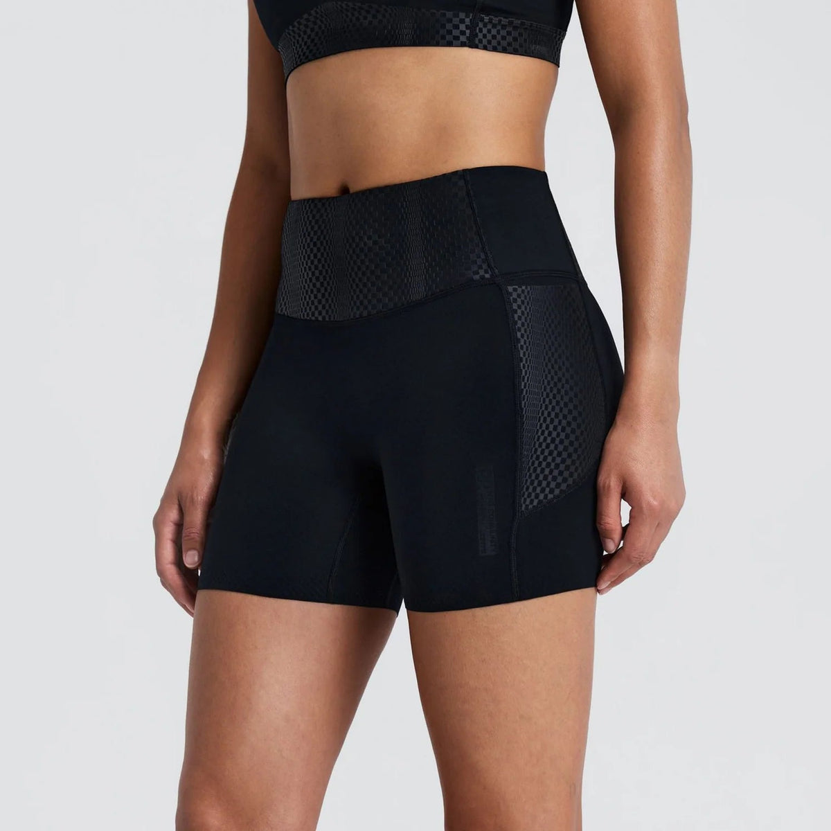 A model wearing black high-waisted athletic shorts with textured side panels, shown from the waist down against a light gray studio background.